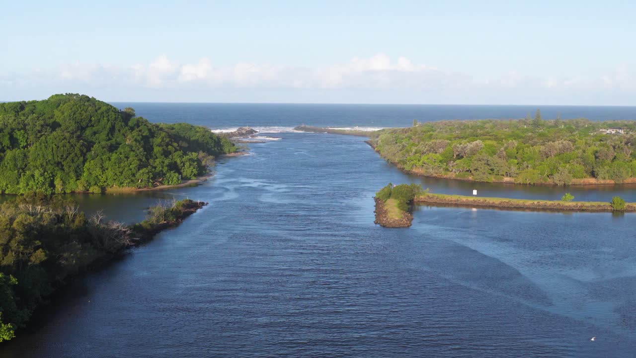 Aerial footage captures a serene river meeting the ocean at Brunswick Heads, NSW, with lush greenery and clear skies