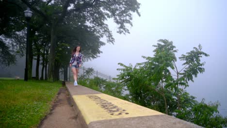 Smiling-girl-walking-on-parapet-in-park.-Woman-going-near-sea