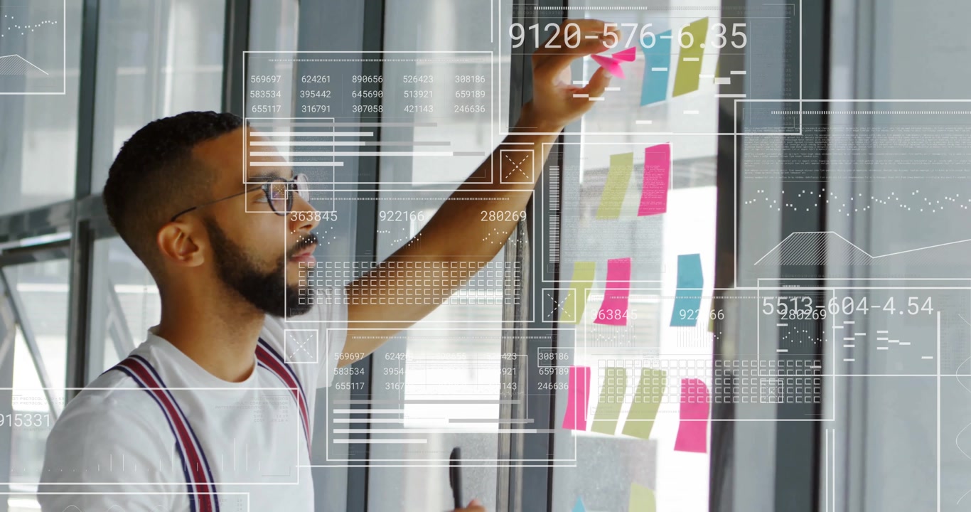 Man scanning note grid and placing sticky notes on glass wall, capturing project planning progress