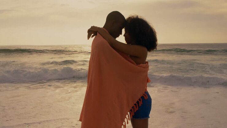 Side view of African American couple wrapped in blanket on the beach 4k