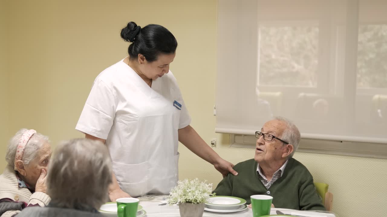 Caregiver talking to senior man in canteen at nursing home