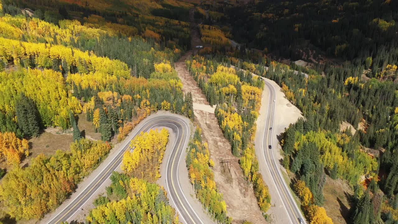 una vista aérea de un sinuoso camino de colorado que serpentea por un valle a través de las montañas y cambia de álamo temblón en otoño