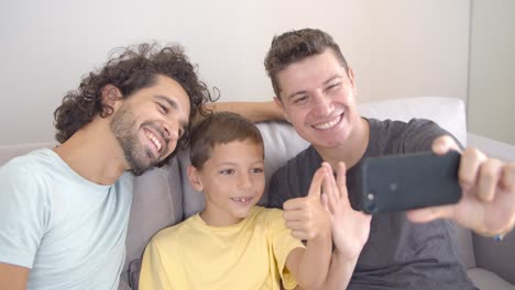 padres gay alegres y un niño usando un teléfono celular para una videollamada