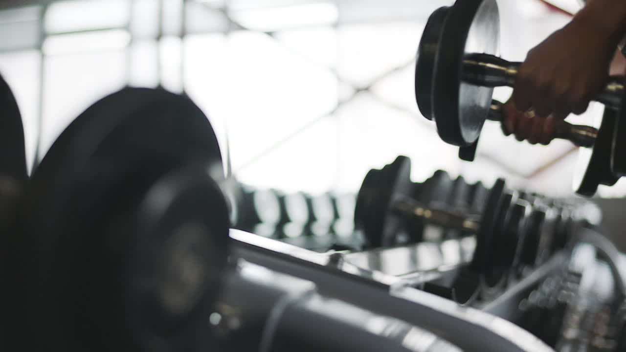Female hands taking bodybuilding dumbbells in gym club.