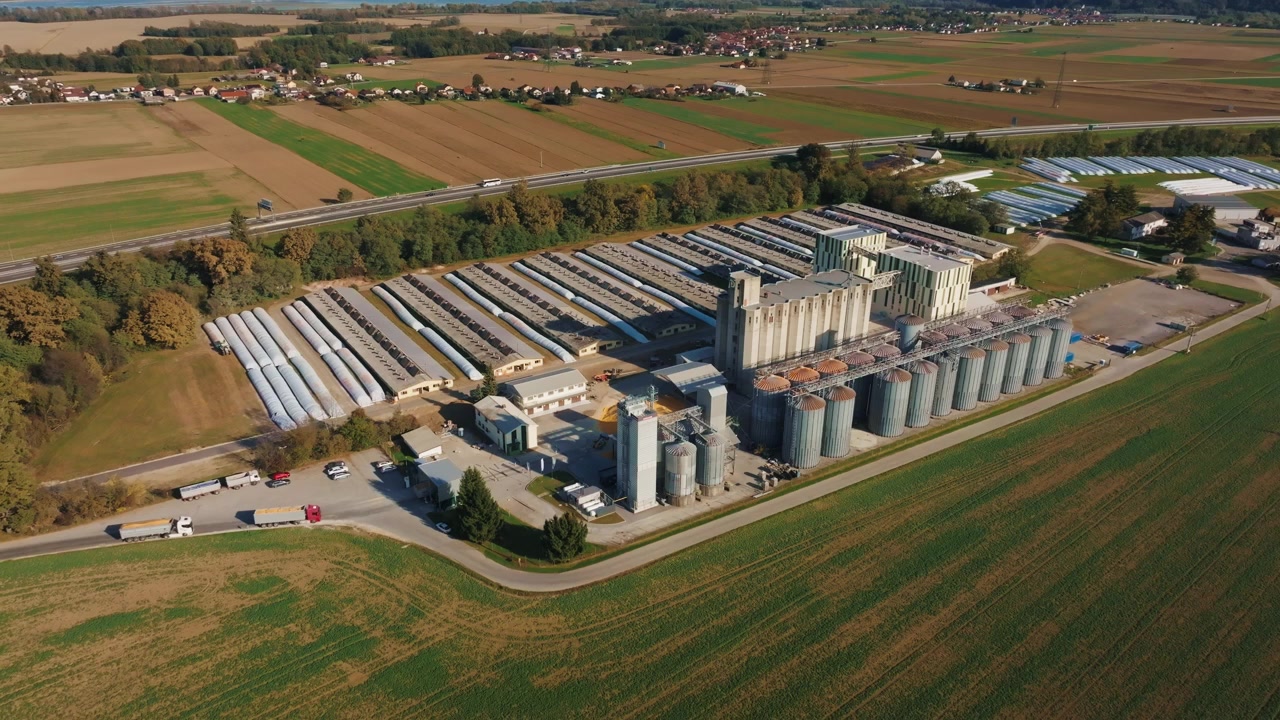 Eine Luftaufnahme zeigt Getreidesilos in einer landwirtschaftlichen Lageranlage, umgeben von Feldern. Lastwagen sind