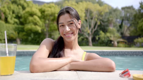 Portrait-of-happy-biracial-teenage-girl-standing-in-sunny-swimming-pool,-slow-motion