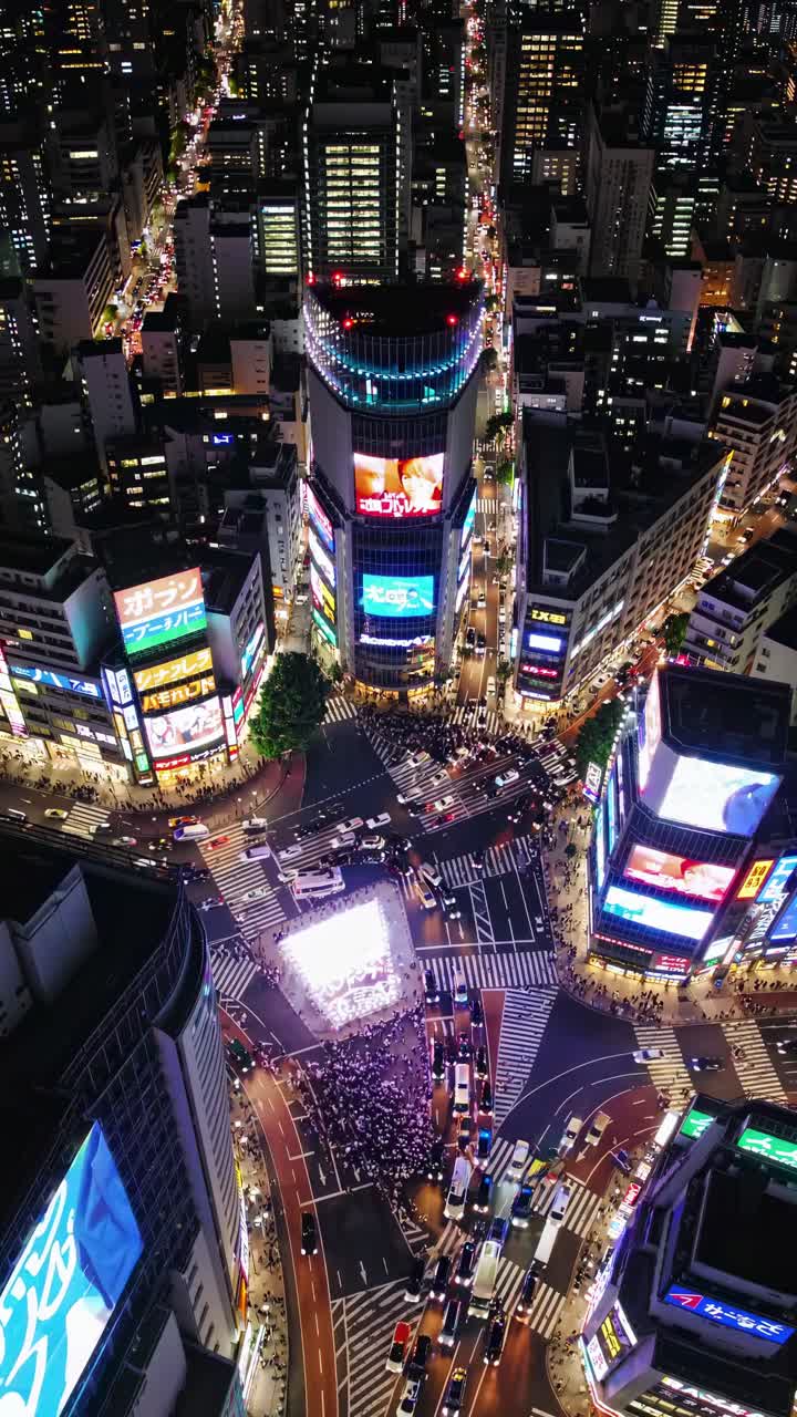 Aerial view of a bustling city intersection at night, illuminated by vibrant neon lights