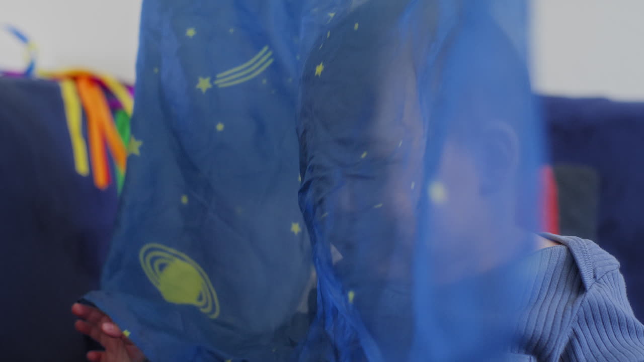 아기가 미소 짓고 웃으며 느린 동작으로 노란색 별과 함께 파란색 실크로 놀고 있습니다.