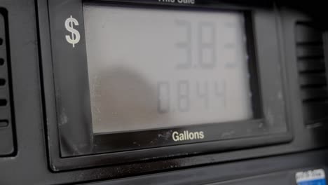 Gas-station-pump-screen-filling-up-and-pumping-slowly-to-5-dollars-and-a-little-over-a-gallon-with-out-of-focus-reflection-of-person-in-screen