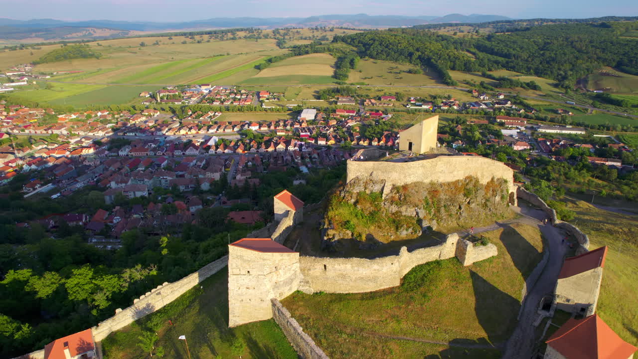 Vista aerea con drone della Fortezza di Rupea al tramonto, Romania. Cittadella situata su una scogliera, turisti, città, vegetazione