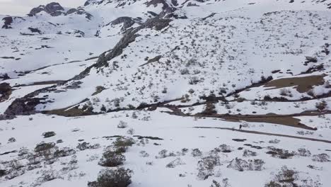 Vista-Aérea-Sobre-Montañas-Nevadas-Y-Excursionista-Caminando-Por-El-Camino-En-Invierno