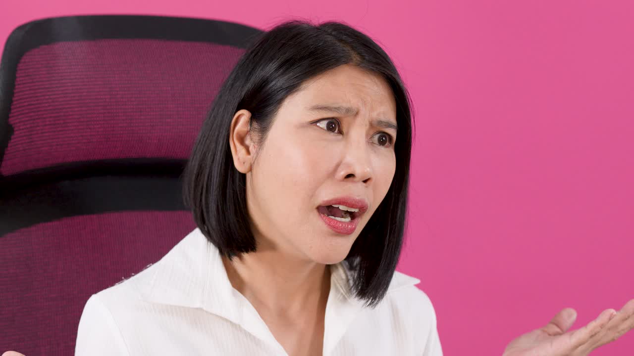 분홍색 배경에서 흰 셔츠를 입은 아시아 여성이 어리둥절한 표정으로 어깨를 으쓱하고 있어요