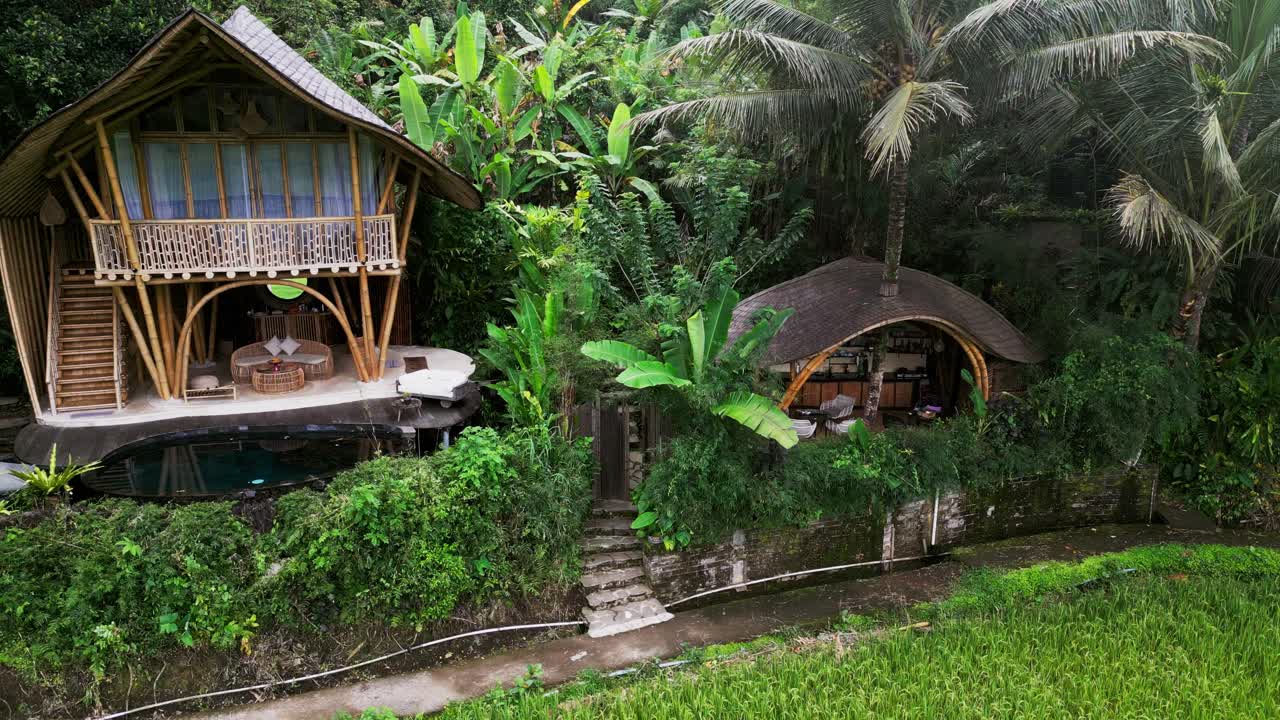 Drone footage capturing a luxury bamboo house in Sidemen Bali nestled within lush tropical vegetation, peaceful gardens, and scenic rice terraces, showing sustainable living and tranquil atmosphere
