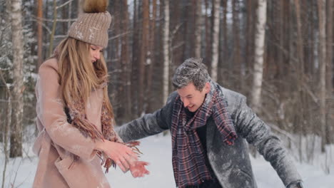 happy couple is playing winter game outside enjoying sunlight and warm winter weather in the mountains. strong boy is carrying girlfriend on his shoulders and whirls her