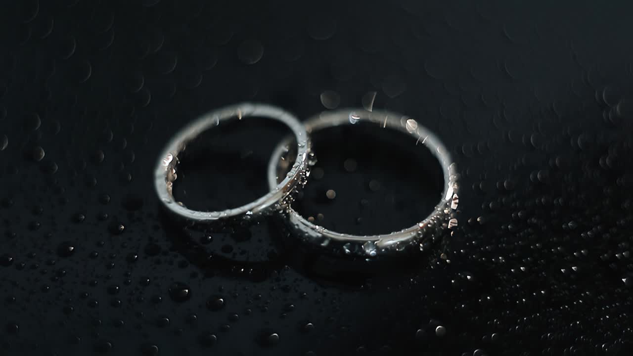 Beautiful wedding rings on a dark, wet surface. Cool light is reflected in the drops. Wonderful shots