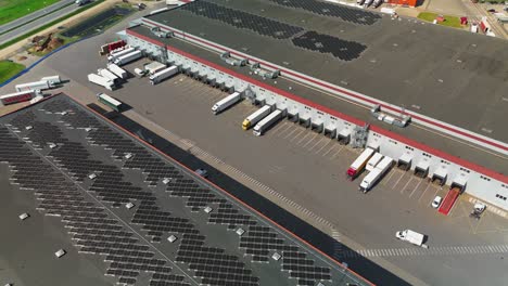 aerial view of a large logistics and distribution center with trucks docked at loading bays. the facility features solar panels on the roof, highlighting a focus on sustainability infrastructure.