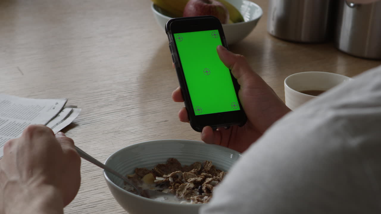 hombre usando un teléfono inteligente con pantalla verde y tomando el desayuno