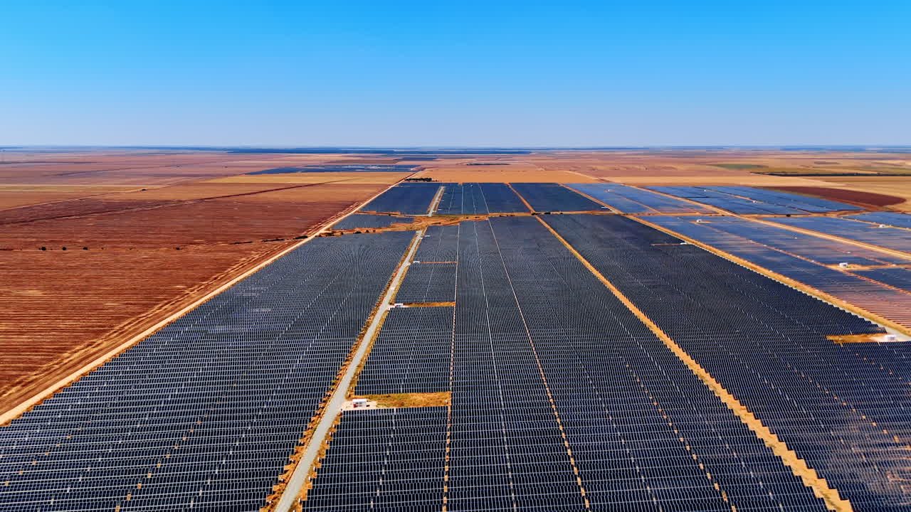 Large solar power station in open landscape. Rows of solar panels stretch across a wide dry landscape under a clear blue sky