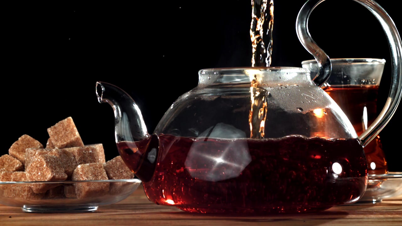Hot Tea Pouring into a Transparent Glass Teapot with Brown Sugar