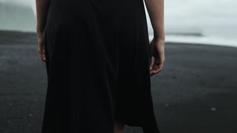 pies caminando por la playa de arena negra, islandia, hermosa mujer pelirroja en vestido negro, seguimiento en cámara lenta, paisaje marino dramático