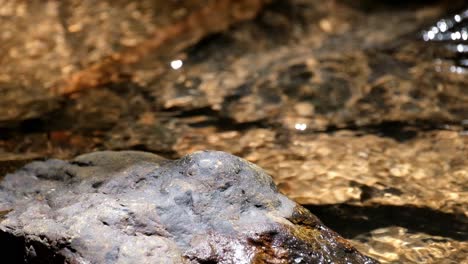 A-rock-then-a-stream-flowing-while-ripples-reflect-sunlight,-Kaeng-Krachan-National-Park,-Thailand