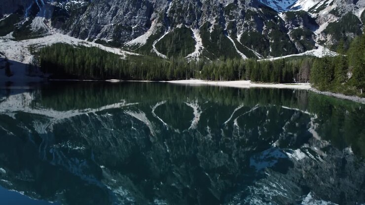 Cime Montuose Innevate che Sovrastano un Sereno Lago Alpino Circondato da una Fitta Foresta