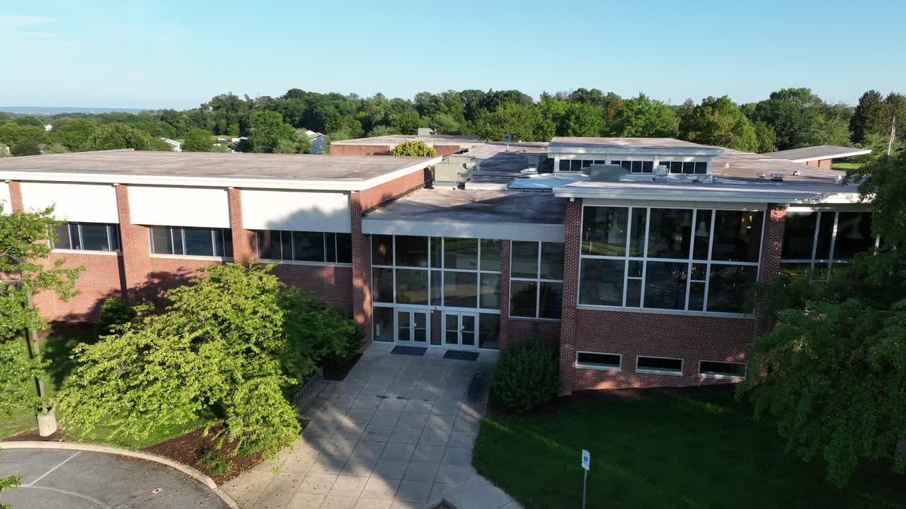 Entrance of brick school in Lititz, Pennsylvania. Aerial descend shot. Empty handrails parking lots. Sunset time in summer. Closed school building