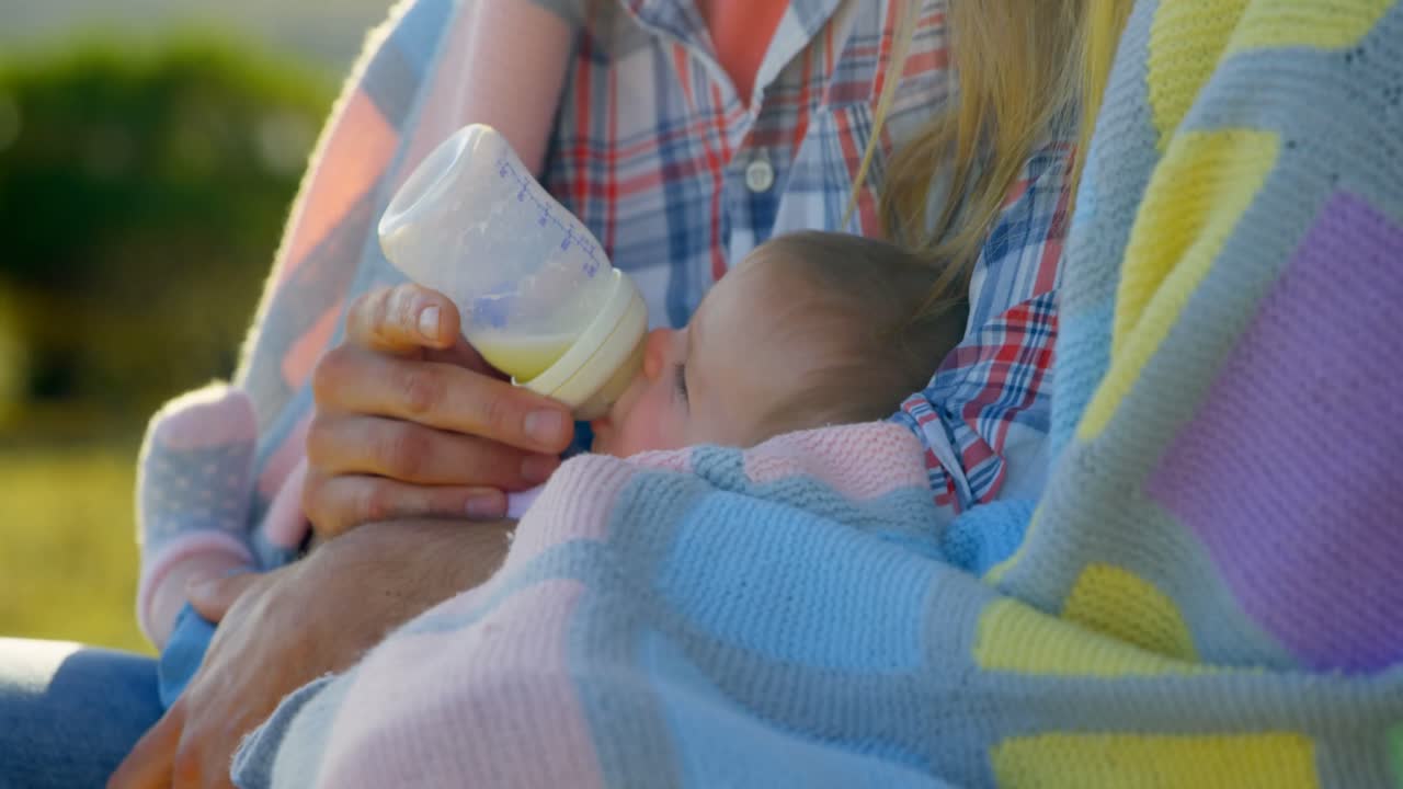 primer plano de padres caucásicos adultos alimentando a su bebé con una botella en el patio trasero de la casa 4k