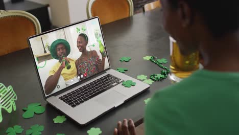 Lächelndes-Afroamerikanisches-Paar-Mit-Bier-Und-Kleeblattförmigen-Gegenständen-Bei-Einem-Videoanruf-Auf-Dem-Laptop