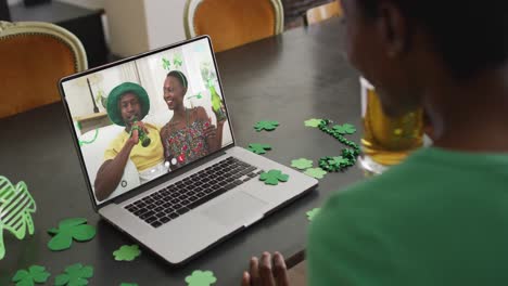 una pareja afroamericana sonriente con cerveza vistiendo artículos en forma de trébol en una videollamada en una computadora portátil