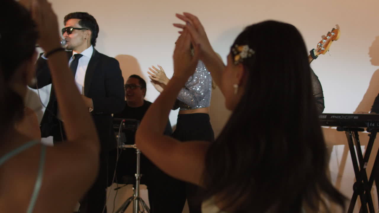 Clip of an elegant party where women in formal dresses enjoy live music. A band can be seen livening up the event.