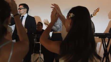clip of an elegant party where women in formal dresses enjoy live music. a band can be seen livening up the event.