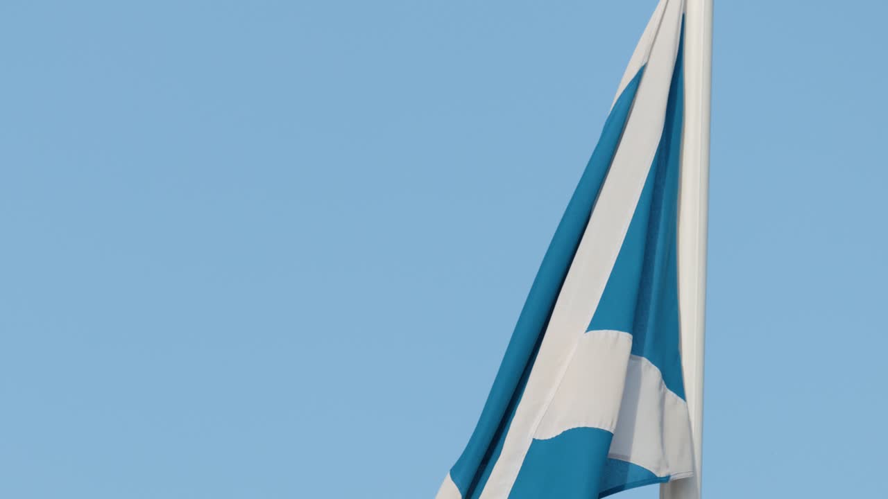 Det skotske flag vajer blidt på en flagstang, dagslys, klar himmel, statisk kamera, minimal komposition