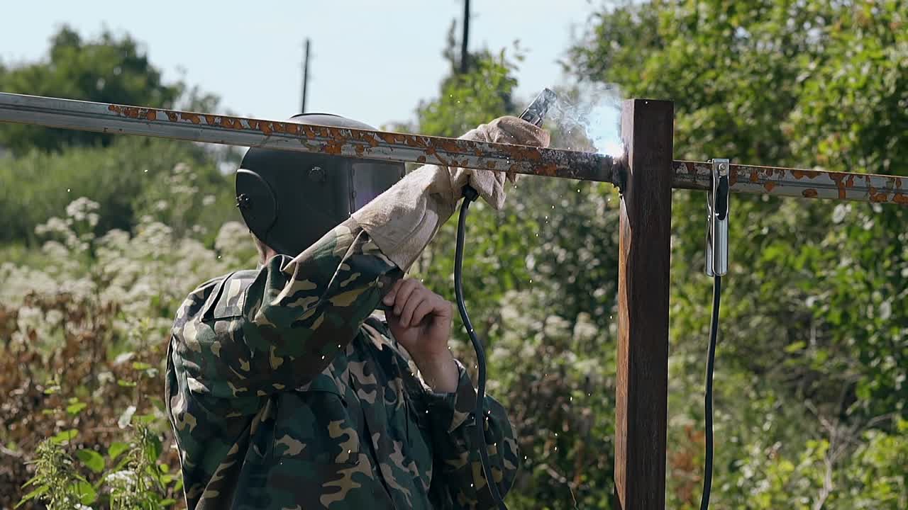 천천히 움직이는 작업자 는 울타리 를 용접 하고 완성 된 작업 을 본다