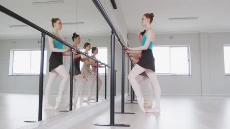 caucasian ballet female dancers exercising together with a barre by a mirror during a ballet class