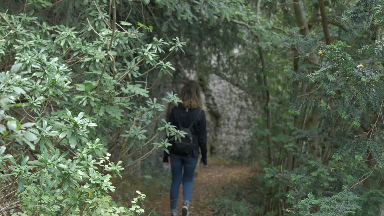 Caucasian girl walking through evergreen forest with rock cliff backdrop