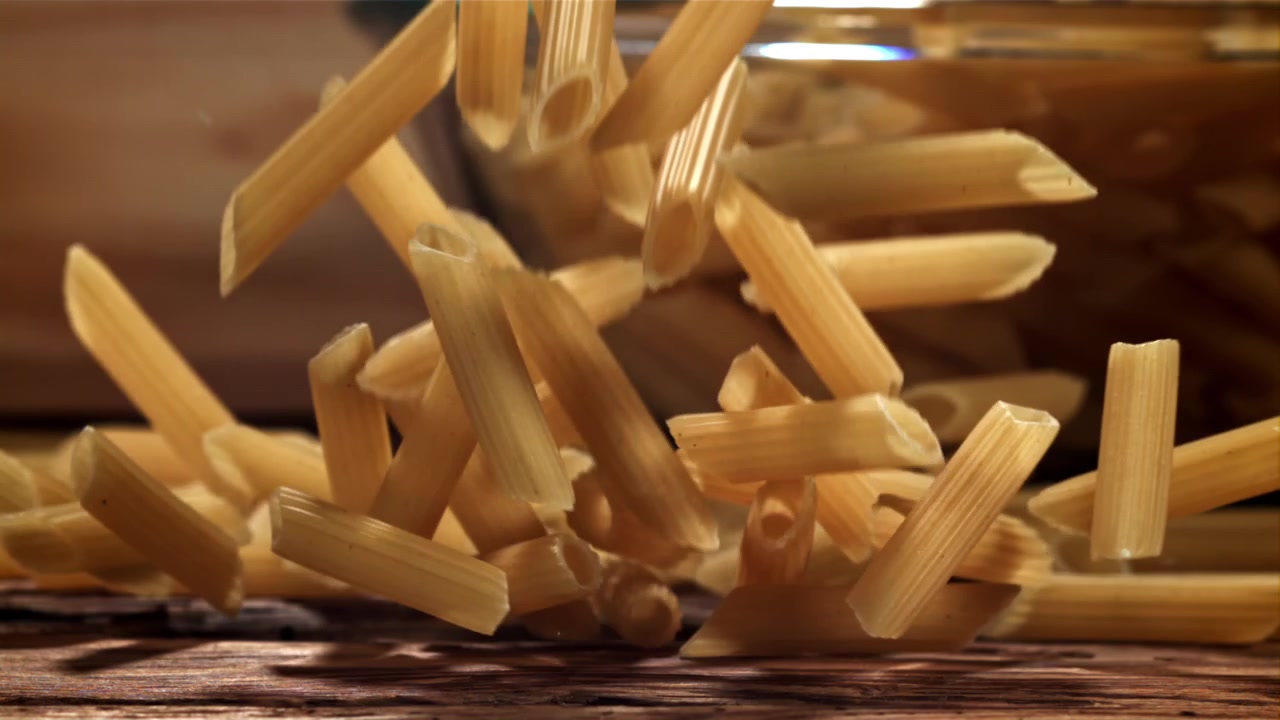 Penne secche che cadono al rallentatore su un tavolo di legno rustico
