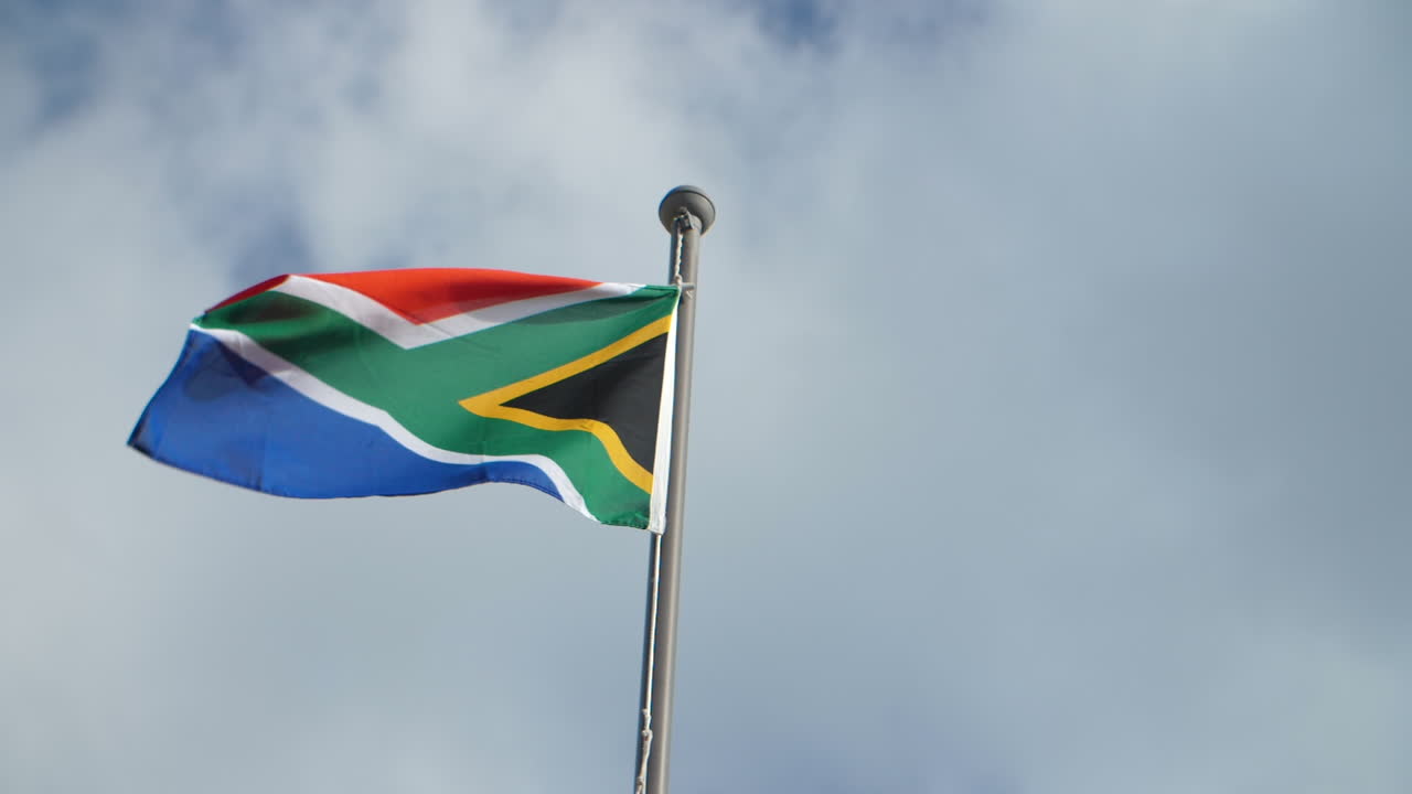 South African flag waving in the wind against cloudy blue sky backdrop on sunny day