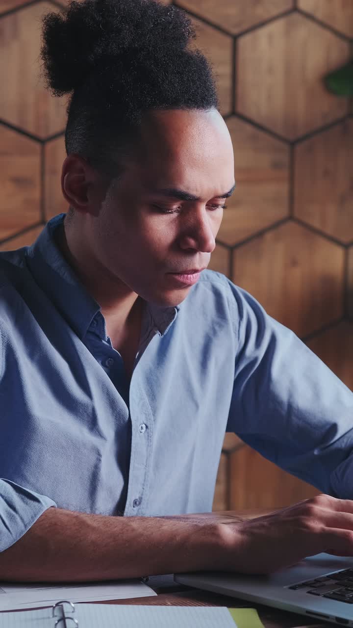 Young focused african american business man uses laptop sits at desk in office