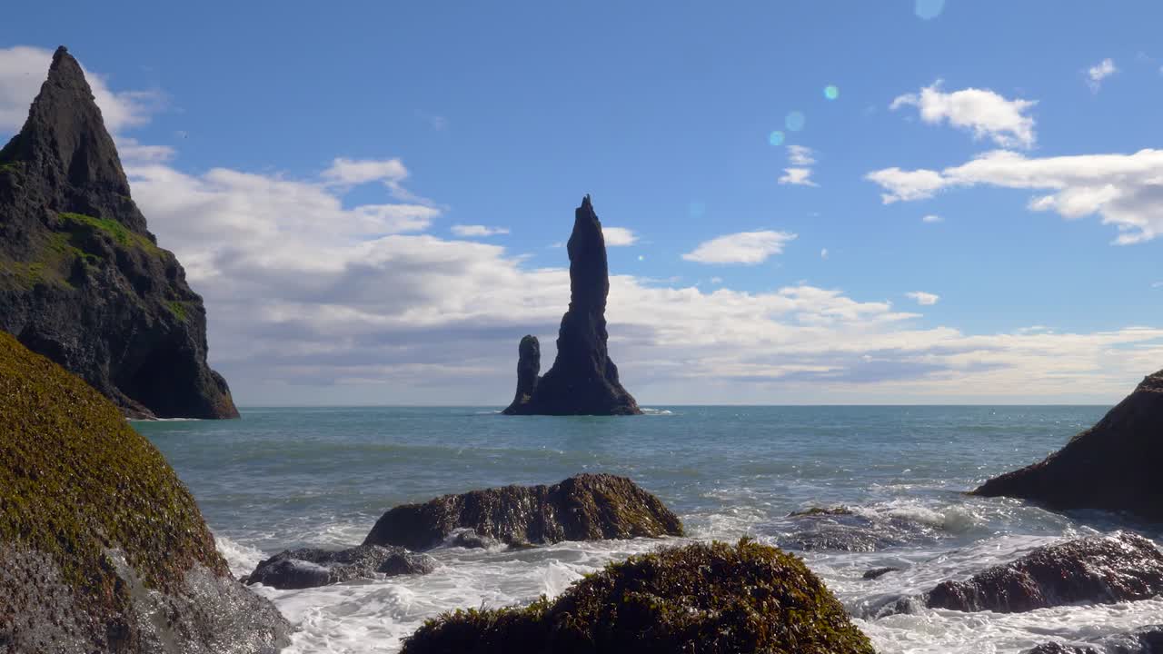 Iconic Reynisfjara black beach spires in distance as ocean waves crash on rocks, iceland