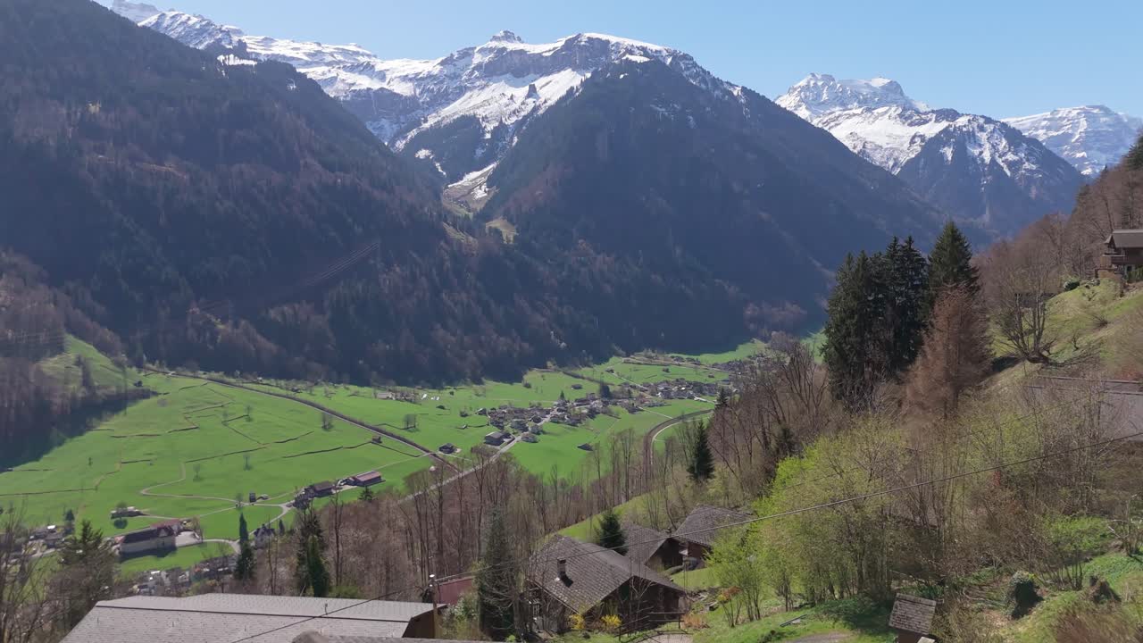 Villaggio alpino di Luchsingen, Schlattberg, Svizzera con montagne innevate sullo sfondo. Ripresa aerea in avanti con inclinazione verso l'alto.