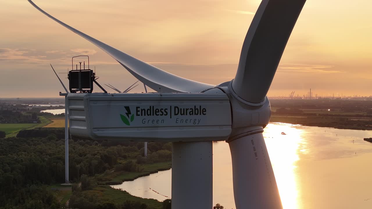 Wind turbine close-up at sunset with "Endless Durable Green Energy" branding above a river