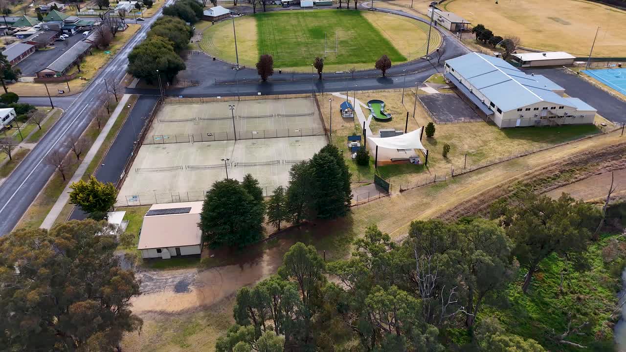 Drone footage glides above local sports courts, playground, and community buildings in a residential neighborhood, with natural daylight and smooth camera movement
