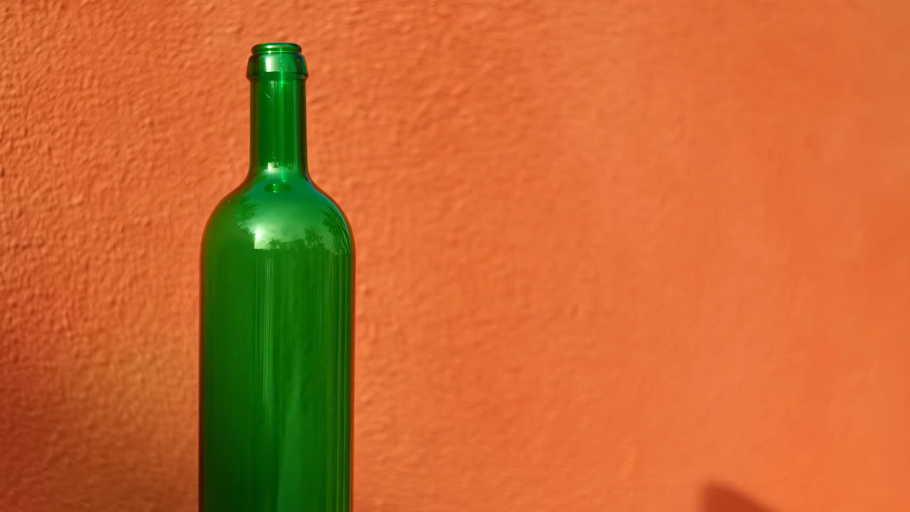 Bottiglia verde contro parete arancione, natura morta minimalista illuminata dal sole con bottiglia di vino verde lucida che proietta una luce soffusa