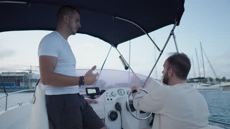 two men on a boat in a marina, one at the helm