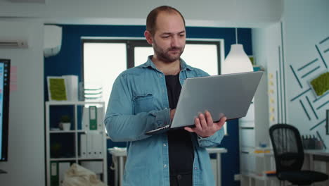 Portrait-of-casual-business-man-holding-laptop-typing-on-keyboard-and-smiling-at-camera