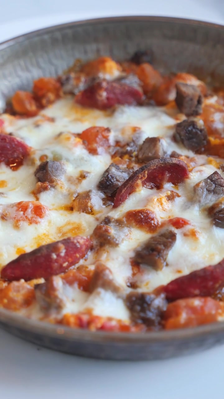 Piatto caldo sfrigolante con formaggio fuso, carne a cubetti e salsiccia