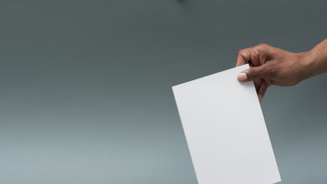 Video-of-hand-of-african-american-man-holding-book-with-blank-page,-copy-space-on-grey-background