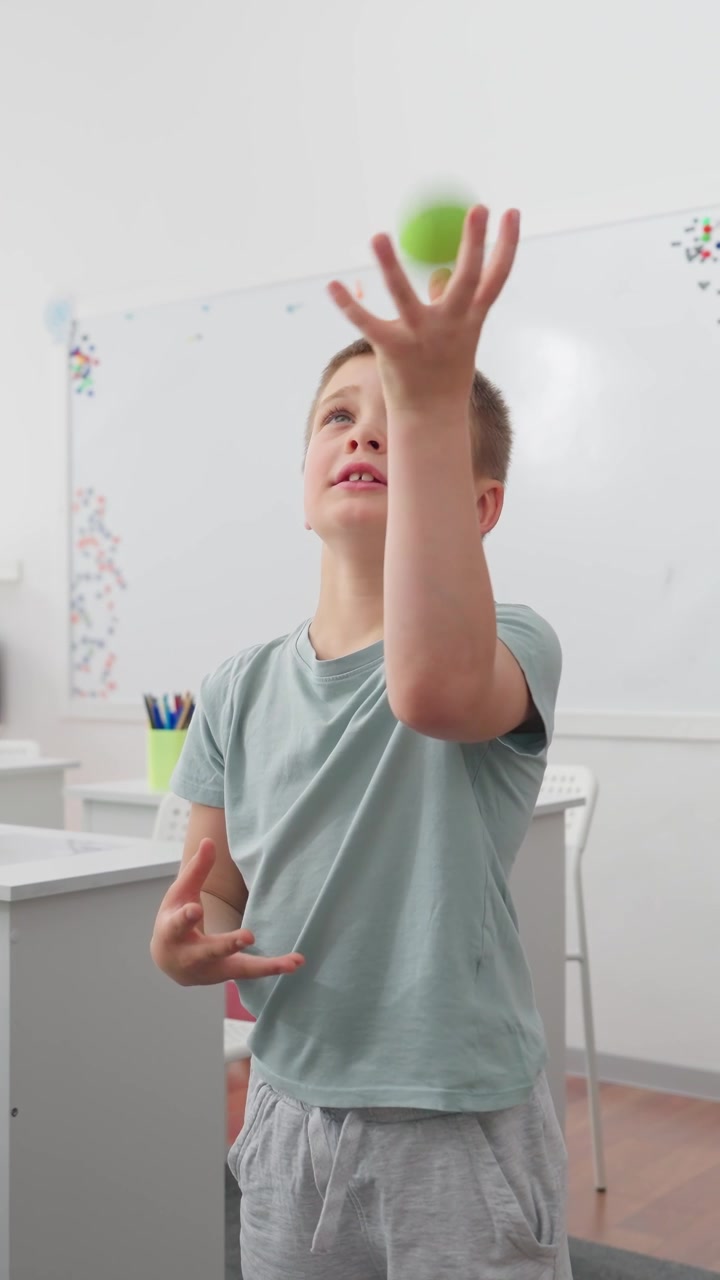 Focused Boy Throws and Catches a Ball in a Classroom