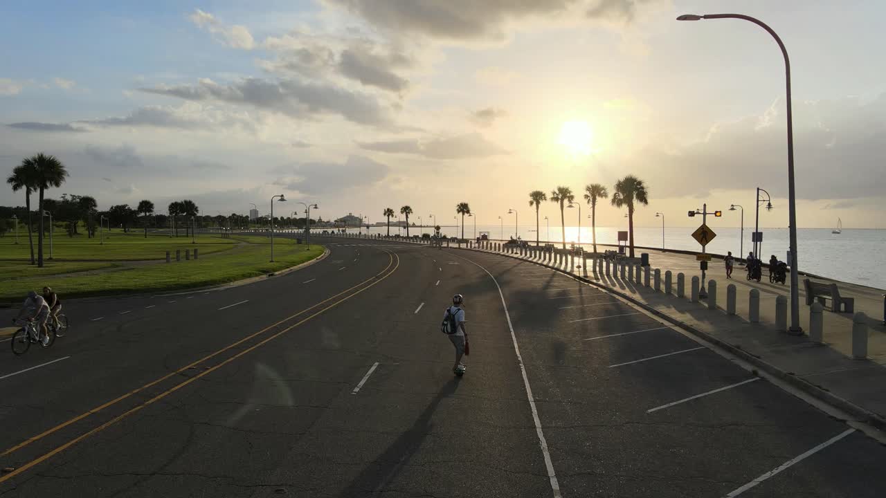 Young Man Riding Electronic Skateboard At Lakeshore Drive During Golden Hour In New Orleans, Louisiana. - aerial follow, rear